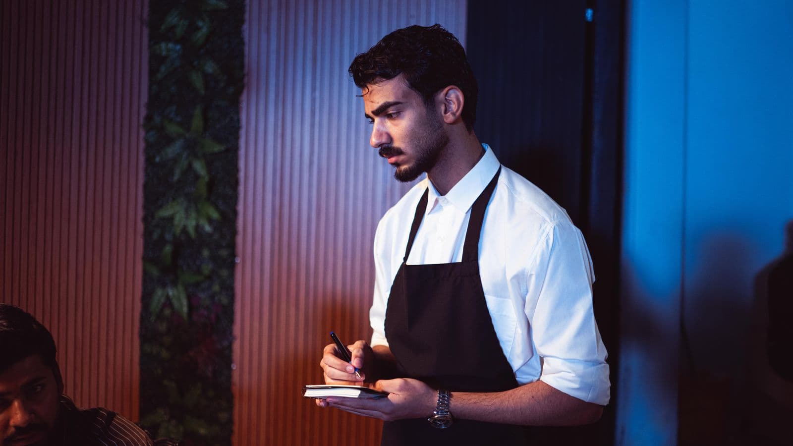 A waiter writing a guest’s request in a small notebook.